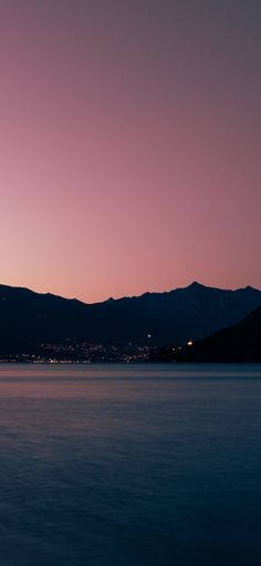 an airplane is flying over the water at night with mountains in the backgroud