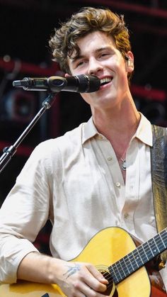 a young man holding a guitar and singing into a microphone