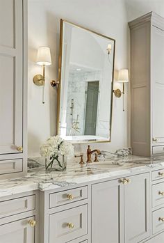 a white bathroom with marble counter tops and gold accents on the mirror above the sink