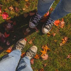 two people standing next to each other in the grass with autumn leaves on the ground