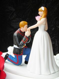 a bride and groom figurine sitting on top of a wedding cake, holding each other's hand