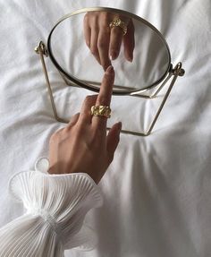 a woman's hand pointing at the bottom of a gold ring on top of a mirror