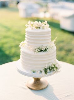 a white wedding cake sitting on top of a wooden table next to a grass covered field