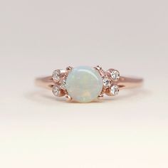 a white opal and diamond ring on top of a plain surface with the center stone surrounded by small diamonds