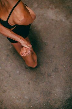 a woman in a black swimsuit standing on the ground with her leg up and hands behind her back