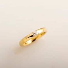 a yellow gold ring with a single diamond on it's side, against a white background