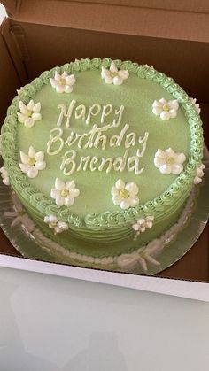 a green birthday cake with white flowers on it in a cardboard box that says happy birthday brenda