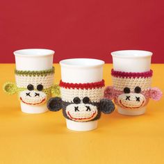 three crocheted cups with monkeys on them and one has a cup holder in the shape of a coffee cup