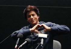 a man sitting at a table with microphones in front of him and making a heart sign