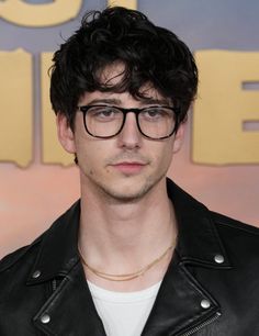 a man wearing glasses and a leather jacket in front of a wall with the words'glee'written on it