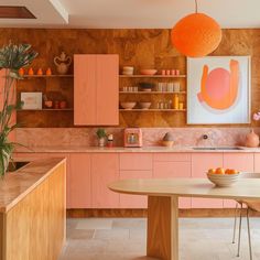 a kitchen with pink cabinets and an orange ball hanging above the countertop, along with a bowl of fruit on the dining room table