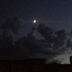 the moon is shining brightly in the sky above some buildings at night with dark clouds