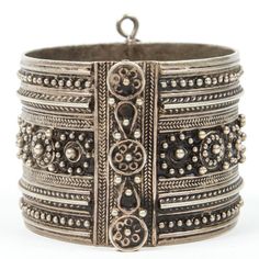 an antique silver bracelet with ornate designs and beads on the outside, set against a white background