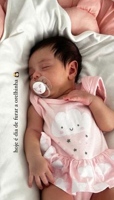 a baby sleeping with a pacifier in its mouth and wearing a pink outfit on it's chest