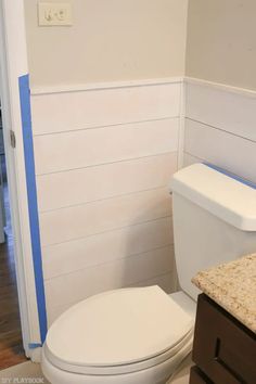 a white toilet sitting in a bathroom next to a wooden cabinet and counter with blue tape on it