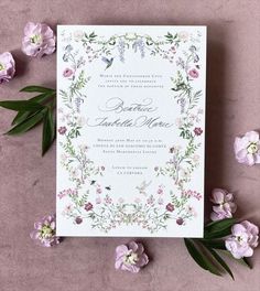 the wedding card is surrounded by flowers and greenery on top of a pink surface