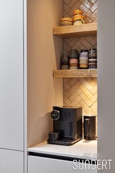 there is a coffee maker on the counter next to some shelves with cups and mugs