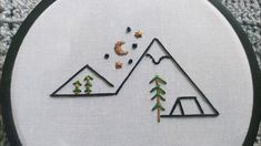 a close up of a embroidery on a piece of cloth with trees and mountains in the background