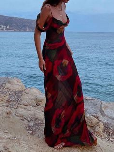 a woman standing on top of a rock next to the ocean wearing a red and black dress