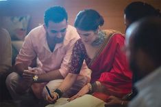 a man and woman sitting on a couch looking at something in front of them while holding a pen