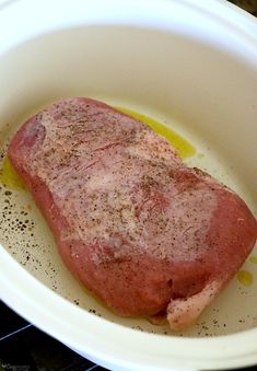 a raw piece of meat in a white bowl on a stove top with oil and seasoning