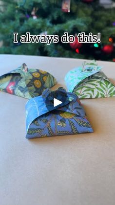 three folded paper bags sitting on top of a table next to a christmas tree with the words, i always do this