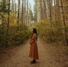 a woman standing in the middle of a dirt road surrounded by tall, thin trees