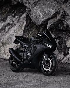 a black motorcycle parked in front of a large rock