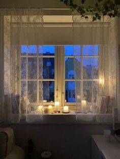 candles are lit on the windowsill in front of an open window with white curtains