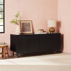 a living room with pink walls and wooden furniture in the corner, including a black credenza sideboard