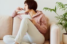 a woman sitting on a couch holding a pen and looking at something in her mouth