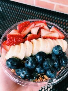 a person holding a bowl of fruit on top of a table