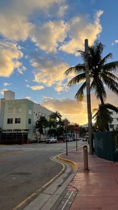 the sun is setting behind palm trees on the side of the road in front of some buildings