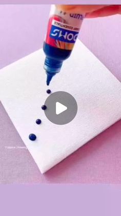 someone is painting something on a piece of white paper with blue dots and a bottle of glue