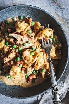 a bowl filled with pasta and peas on top of a table next to a fork