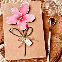 a pink flower on top of a piece of paper next to a marker and brush