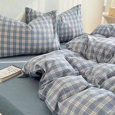 an unmade bed with blue and white plaid comforter, pillows and a book on it