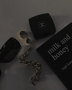 a pair of sunglasses, book and chain on a white surface with the words milk and honey written across it