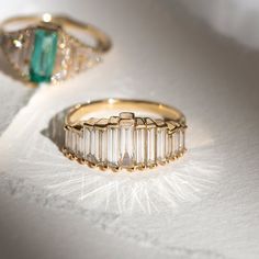 two gold rings with emeralds and diamonds on white surface, close up view from above