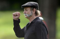 an older man wearing a black hat and holding his fist up