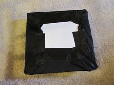 an empty black bag sitting on top of a carpeted floor next to a white piece of paper