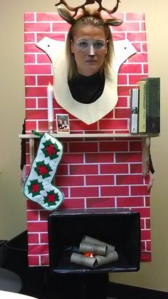 a woman is standing in front of a brick fireplace decorated with christmas stockings and reindeer antlers