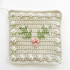 a white crocheted square with green and pink flowers on the front, sitting on a white surface