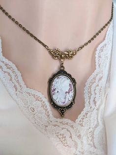 This beautiful vintage-style Cameo necklace features a classic portrait cameo of a Greek Goddess. The cameo has a chalk-white relief on a faded-ruby background. Set in an ornate antique brass pendant that is suspended from a beautiful vintage style floral necklace connector.  A quintessential gift for anyone who loves vintage-inspired Victorian and Gothic jewelry.  Size: The ornate necklace pendant is silver-plated brass and measures 40 mm (1 1/2 inches) long, and 24 mm (just under 1 inch) wide. Vintage Cameo Jewelry For Wedding, Antique Gold Cameo Pendant Necklace, White Vintage Necklaces For Vintage Events, White Vintage Necklace For Vintage Collection, Vintage White Necklaces, White Vintage Necklace, Classic Cameo Necklace As Gift, Vintage Cameo Medallion Necklace, Classic Cameo Necklace For Gift