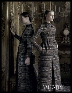 two women standing next to each other in front of a wall with ornate designs on it