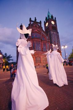 three people dressed in white are walking down the street with large buildings behind them at night