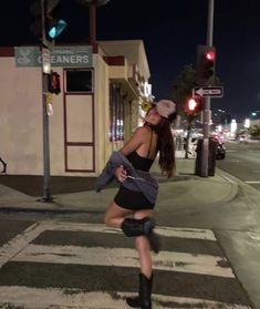 a woman in short shorts and boots is crossing the street