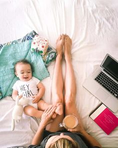 a woman laying on top of a bed holding a baby next to a laptop computer