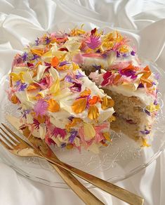 a cake with white frosting and colorful flowers on it next to a gold fork