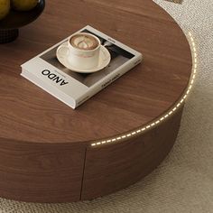 a coffee table with a book, bowl of fruit and cup of coffee on it